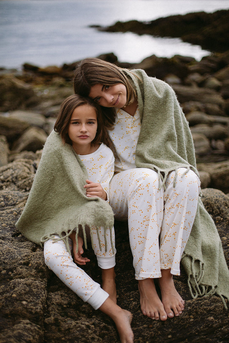 a girl and a woman sat on a rock at the sea side wearing organic sleepy doe pyjamas and wrapped in a blanket