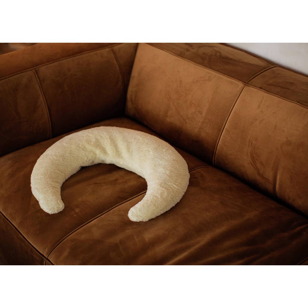 White crescent-shaped pillow on a brown leather couch