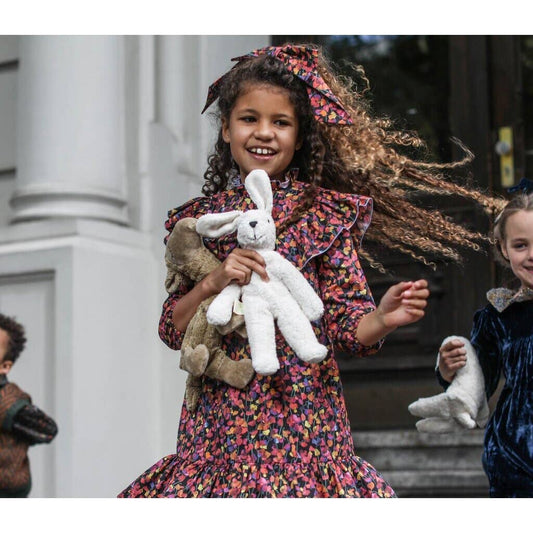 Young girl in a floral dress holding stuffed animals outdoors