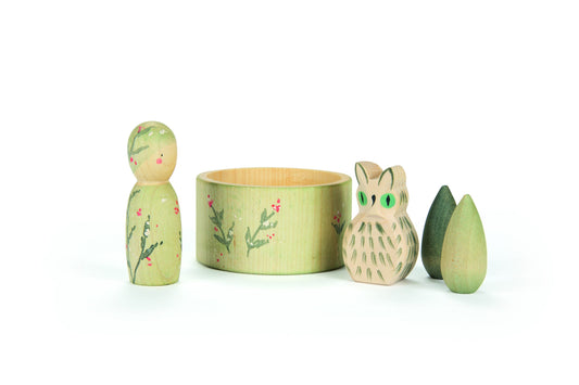 Set of wooden toys including a green peg doll, a round box with floral design, an owl figurine, and a leaf-shaped object on a white background.