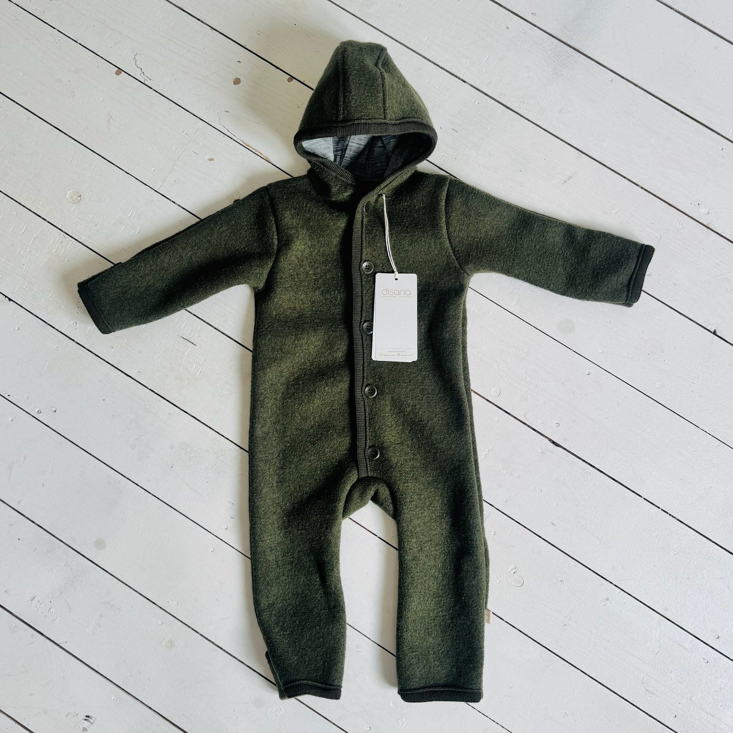 Green baby onesie with a hood on a light wooden floor
