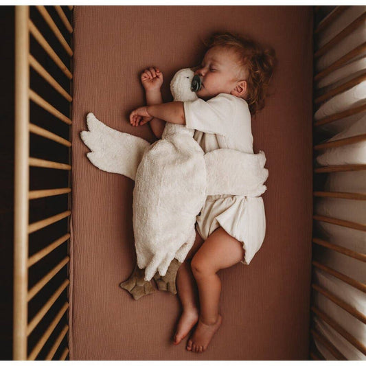 Baby sleeping with a plush swan toy on a brown crib