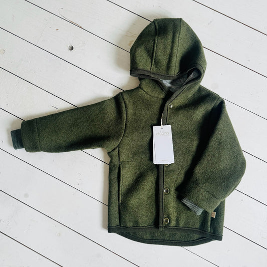 Green children's jacket with a tag on a white wooden floor