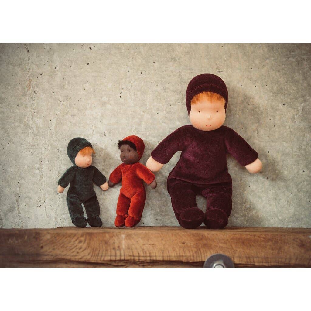 Three dolls in different colored outfits standing on a wooden surface against a textured wall.