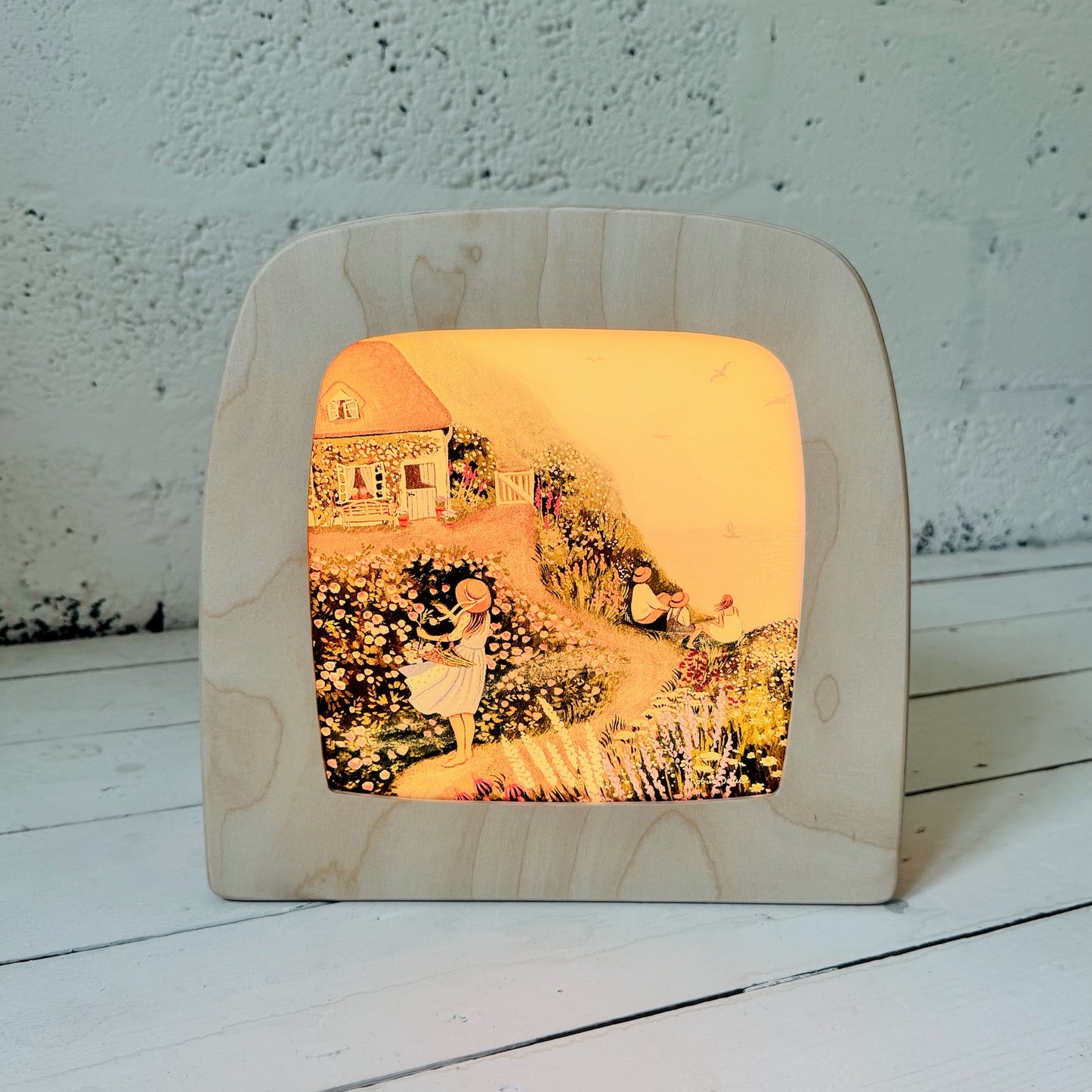Wooden lamp with a printed design of a couple in a garden on a white surface.